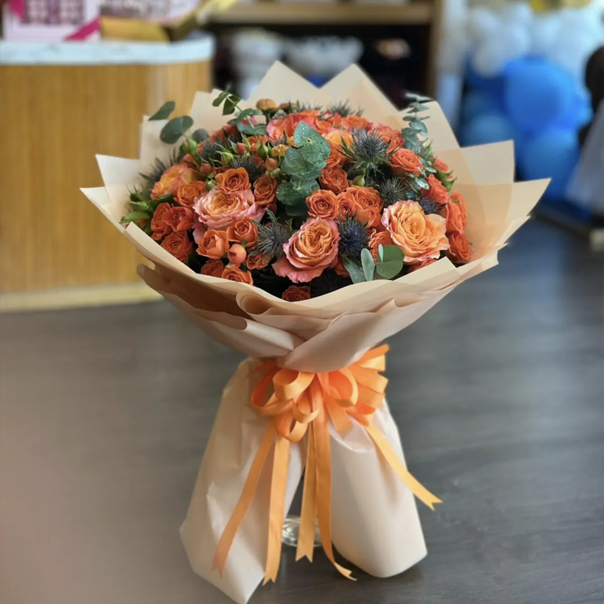 Peach Roses & Thistle Bouquet of orange and peach roses with blue thistle in cream wrapping