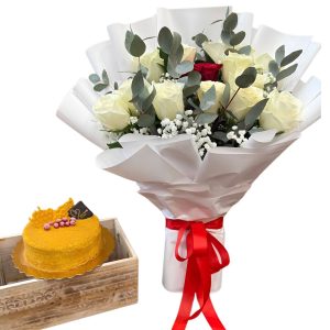 White and red rose bouquet with a round orange-frosted cake in a wooden crate